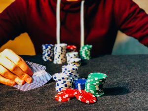 teen in red sweatshirt holds cards with poker chips in front of him, underage gambling is illegal in NJ. 